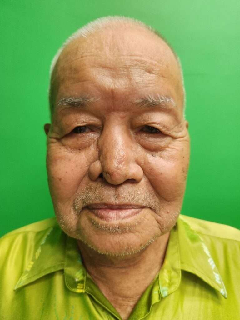 Elderly man smiling against green background.